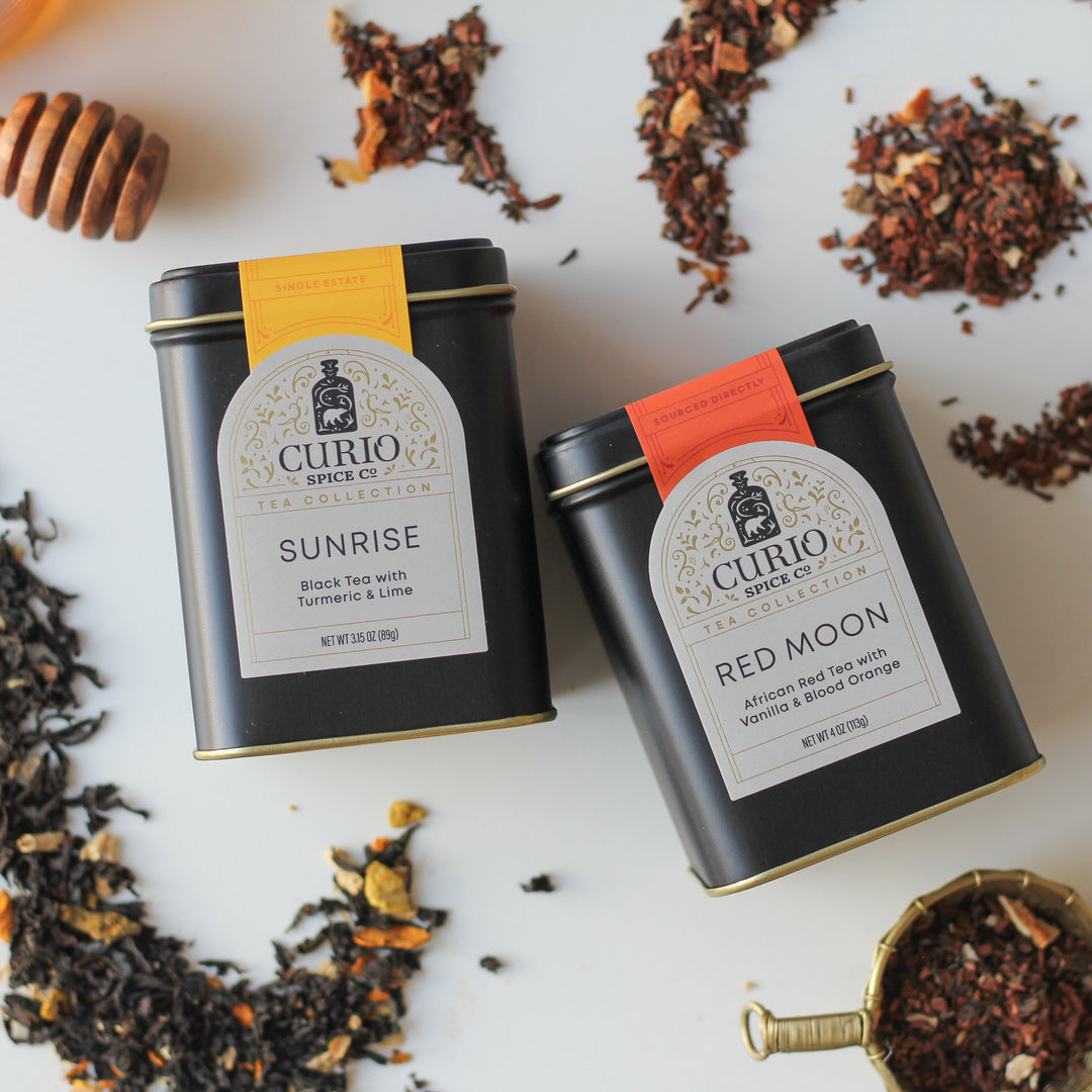 Two Curio Spice Co. tea tins with dried herbs and spices on a white background