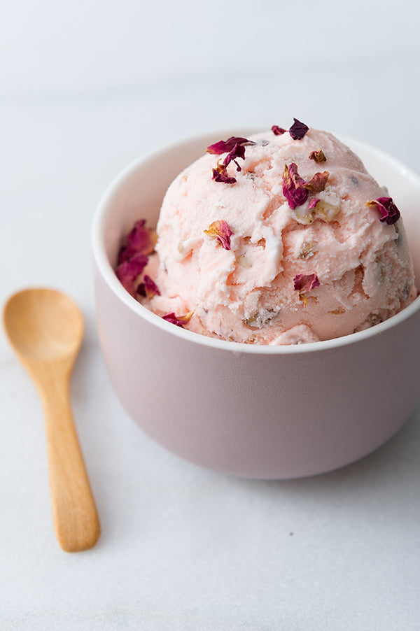 Pink ice cream with rose petals in a white bowl on a light gray background. From  'Malai: Frozen Desserts Inspired by South Asian Flavors' by Pooja Bavishi