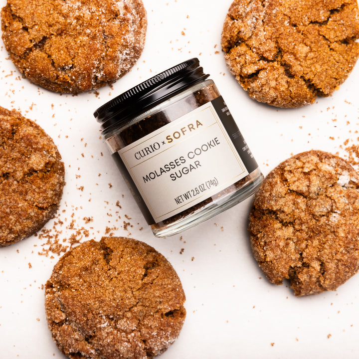 Jar of Curio &amp; Sofra Molasses Cookie Sugar surrounded by cookies on a white background
