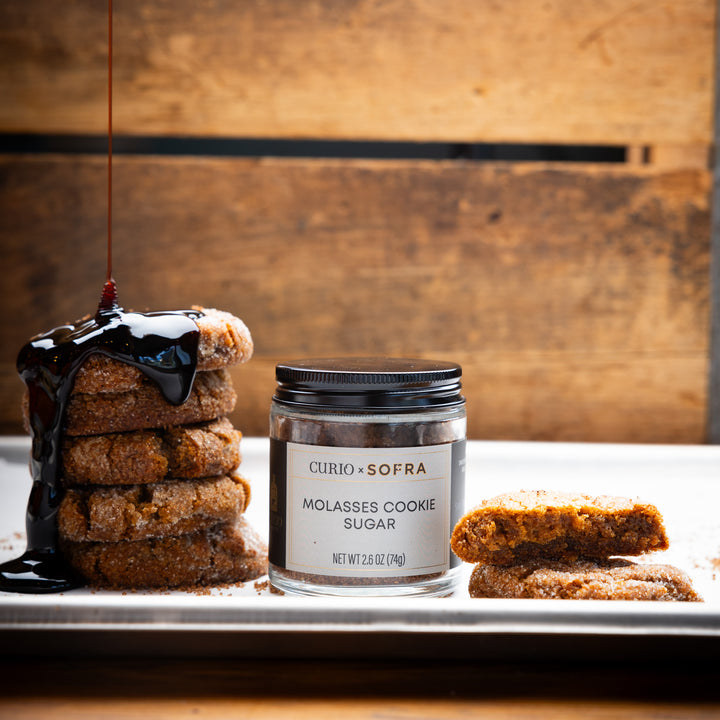 Jar of Curio x Sofra molasses cookie sugar with cookies on a wooden background