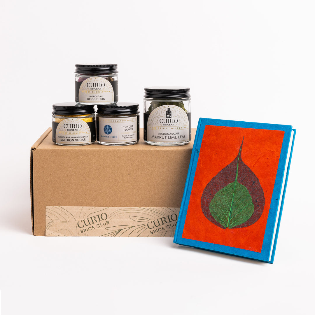 Curio Spice Club spices in a box with a notebook featuring a leaf design on a white background