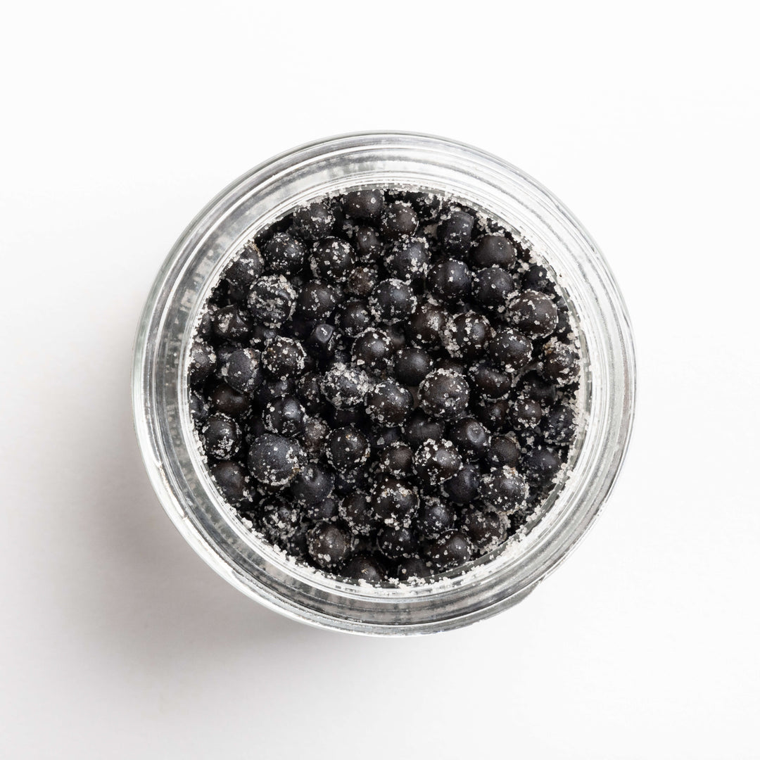Clear jar filled with black peppercorns on a white background