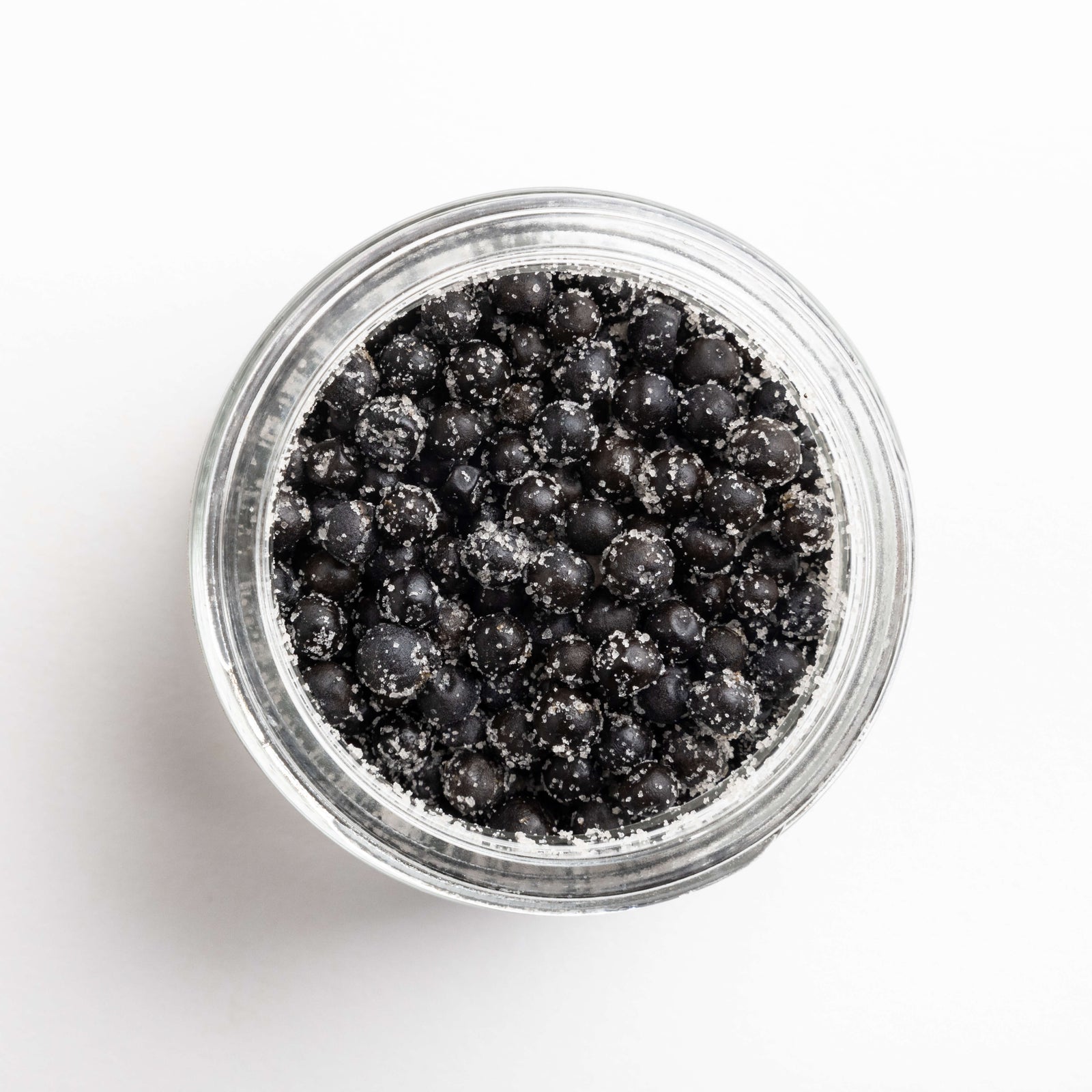 Clear jar filled with black peppercorns on a white background