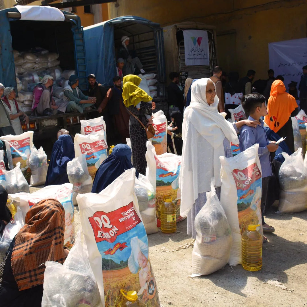People gathered around bags of food and oil at an outdoor distribution event.
