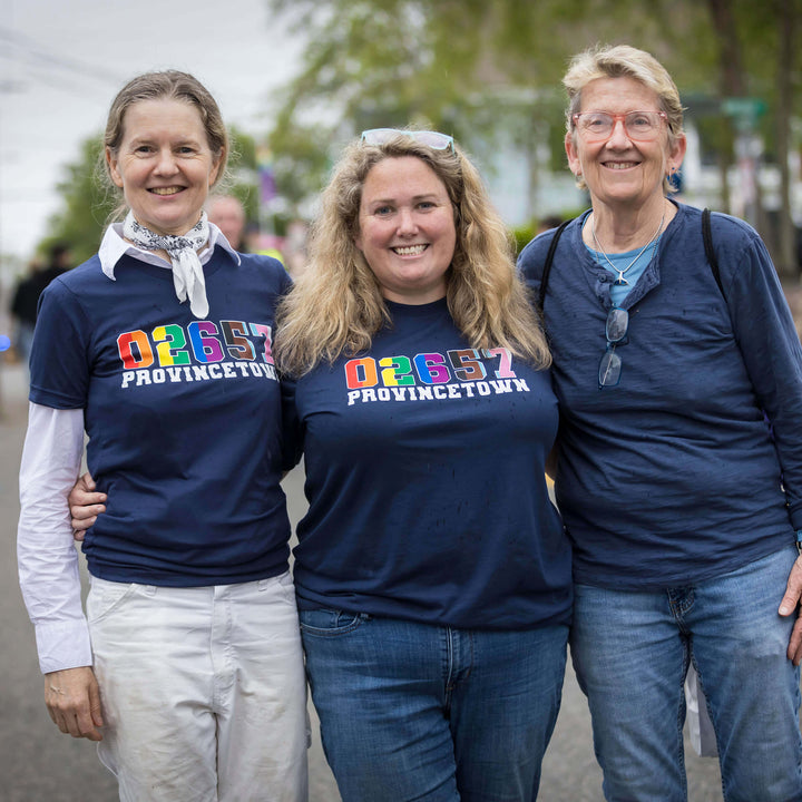 Three women wearing navy blue shirts with colorful text, standing outdoors.
