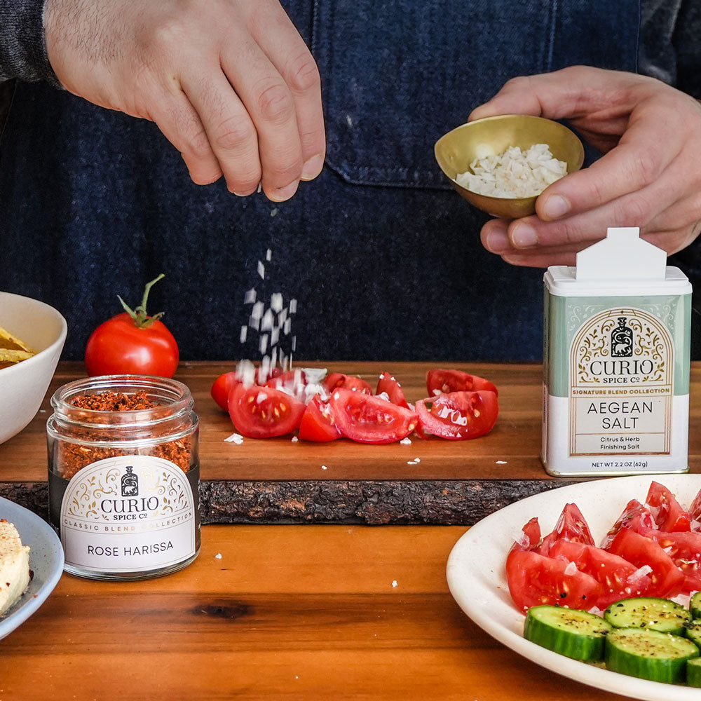Slideshow image of Rose Harissa, Aegean Salt, and Kampot & Salt being sprinkled on hummus and vegetables.