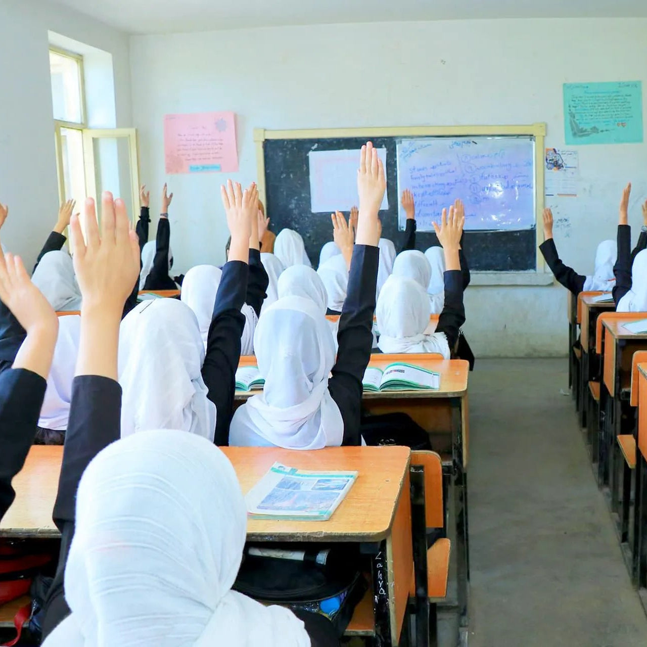 Classroom with students raising hands, wearing white headscarves.