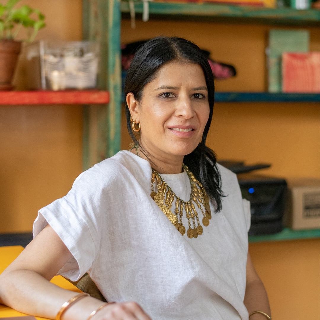 Woman wearing a white shirt and gold jewelry sitting in an office setting.